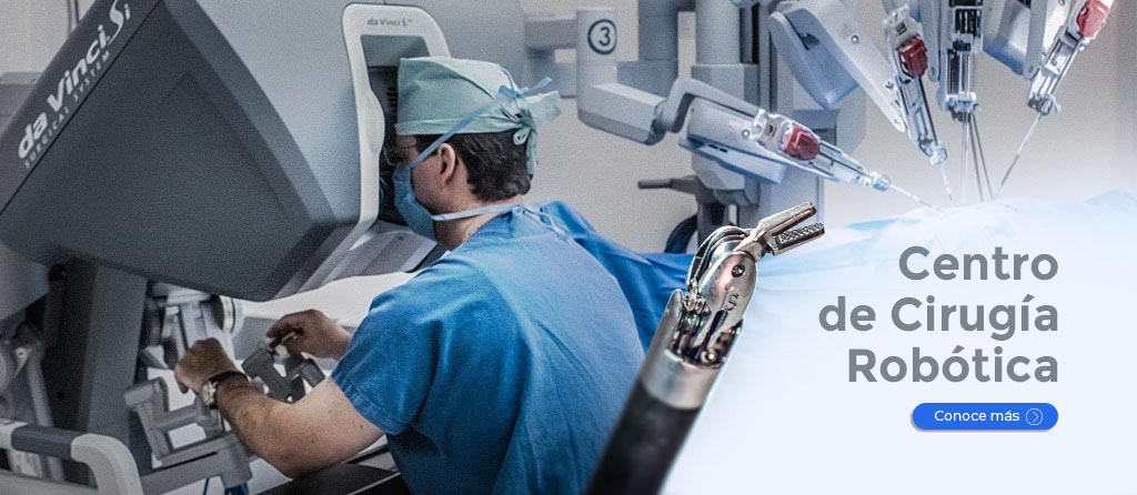Médico sentado frente a la consola del robot quirúrgico, vestido con pijama azul para cirugía y sus manos en los controles.
